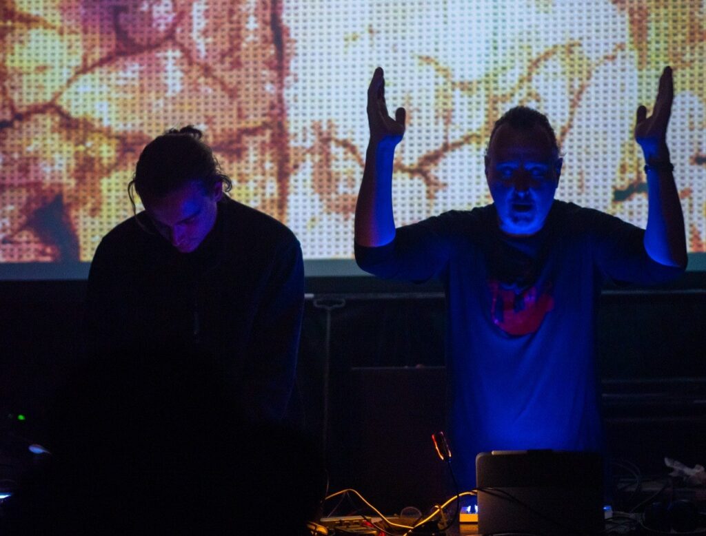 Ur.X live in New York: Uri Killisch mit erhobenen Armen, Enkidu rankX am Rig, davor die Projektionswand — Foto (c) Sulamith Sallmann